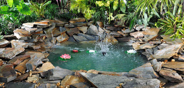 after – pond updated with a waterfall, fountain, beautiful blue water, surrounded by lush tropical greenery and landscaping stones